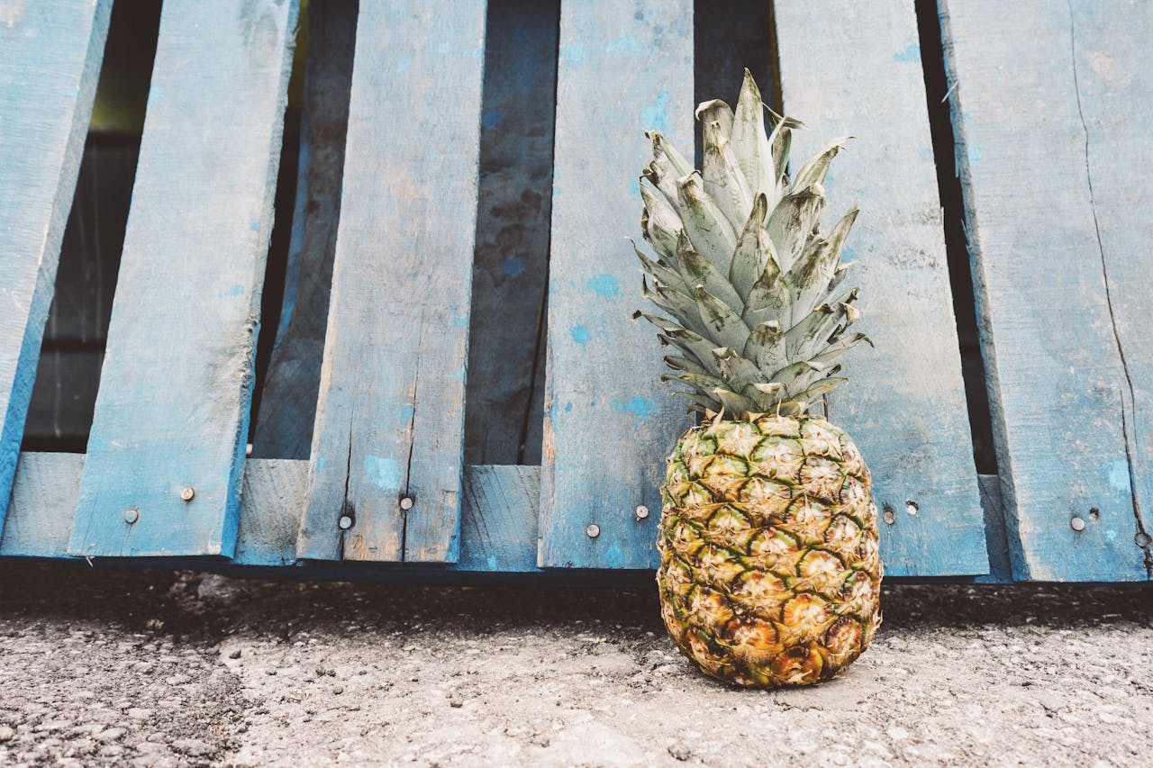 Pineapple resting on the ground against a vibrant blue wooden pallet, captured outdoors.