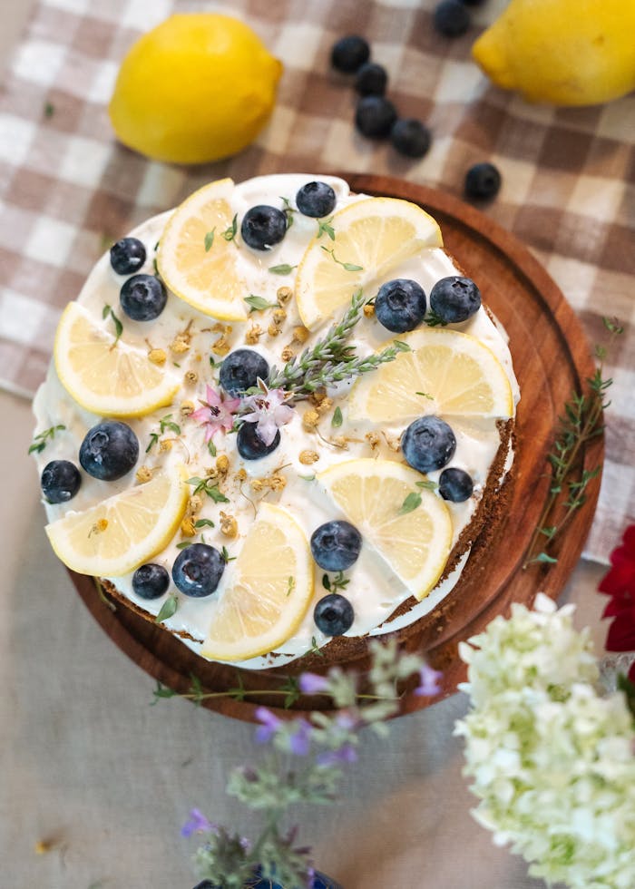 Delicious lemon and blueberry cake garnished with fresh fruits on a wooden platter.